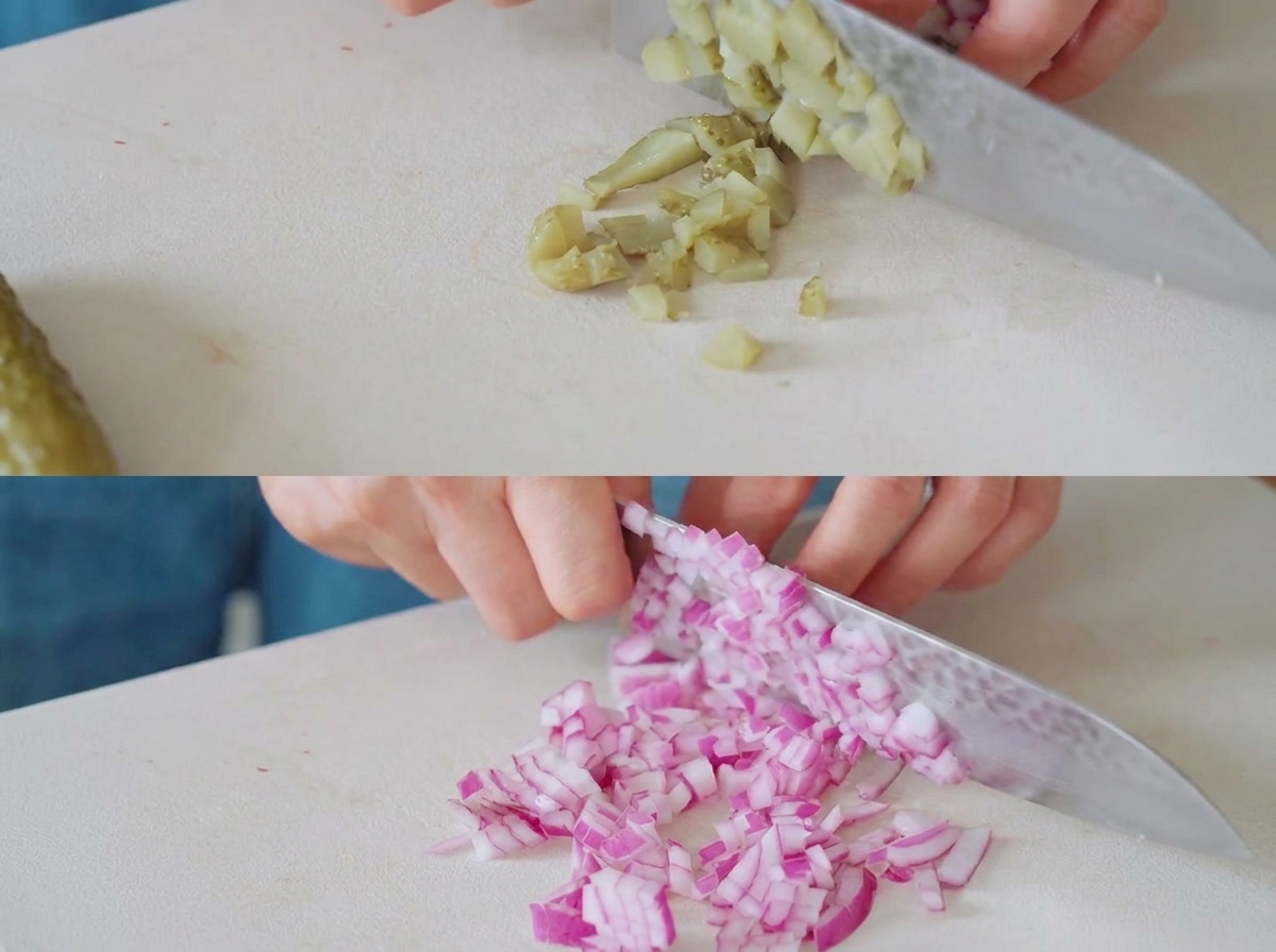 Des cornichons et des oignons rouges coupés en petits morceaux sur une planche à découper blanche avec un couteau de chef.
