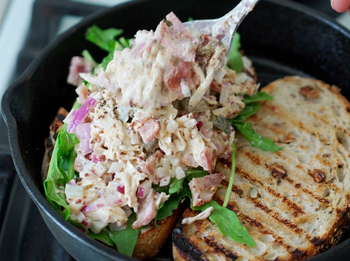 Une cuillerée de salade de poulet effiloché placée sur de la roquette verte fraîche sur une tranche de sandwich au levain.