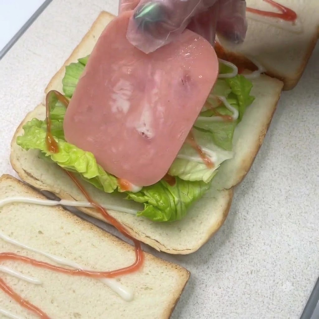 Une tranche de jambon posée sur une couche de laitue sur un morceau de pain de sandwich avec des assaisonnements.