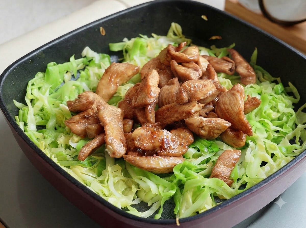 Des lamelles de blanc de poulet cuites placées sur le chou émincé dans la poêle, divisées en deux portions.