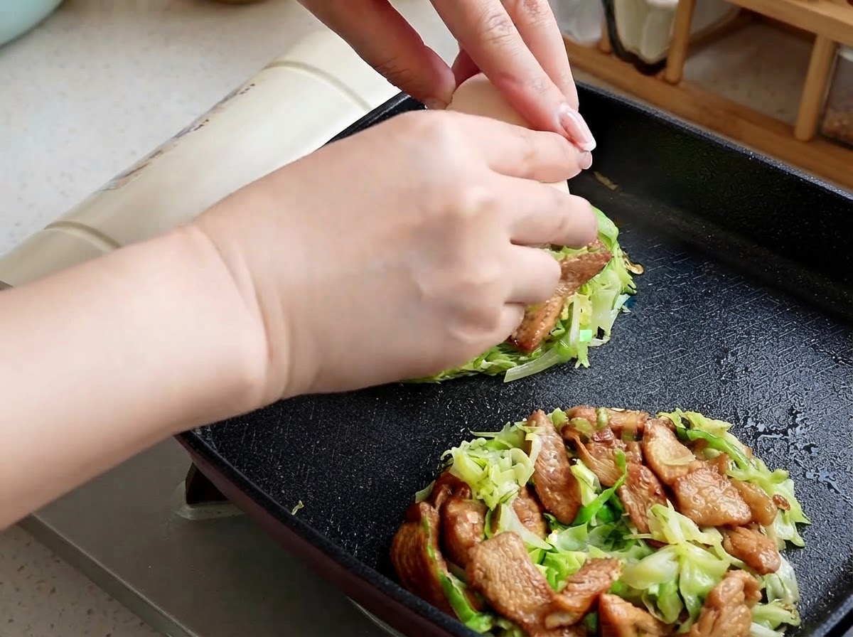 Des mains cassant un œuf cru au centre dune portion de chou et de poulet dans une poêle.