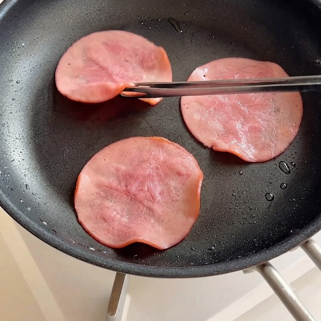 Des tranches de jambon retournées dans une poêle à laide de baguettes.