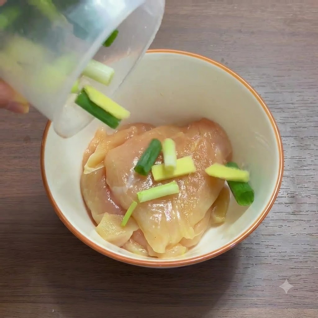 Gros plan de morceaux de blanc de poulet dans un bol mélangés avec des oignons verts et des tranches de gingembre.