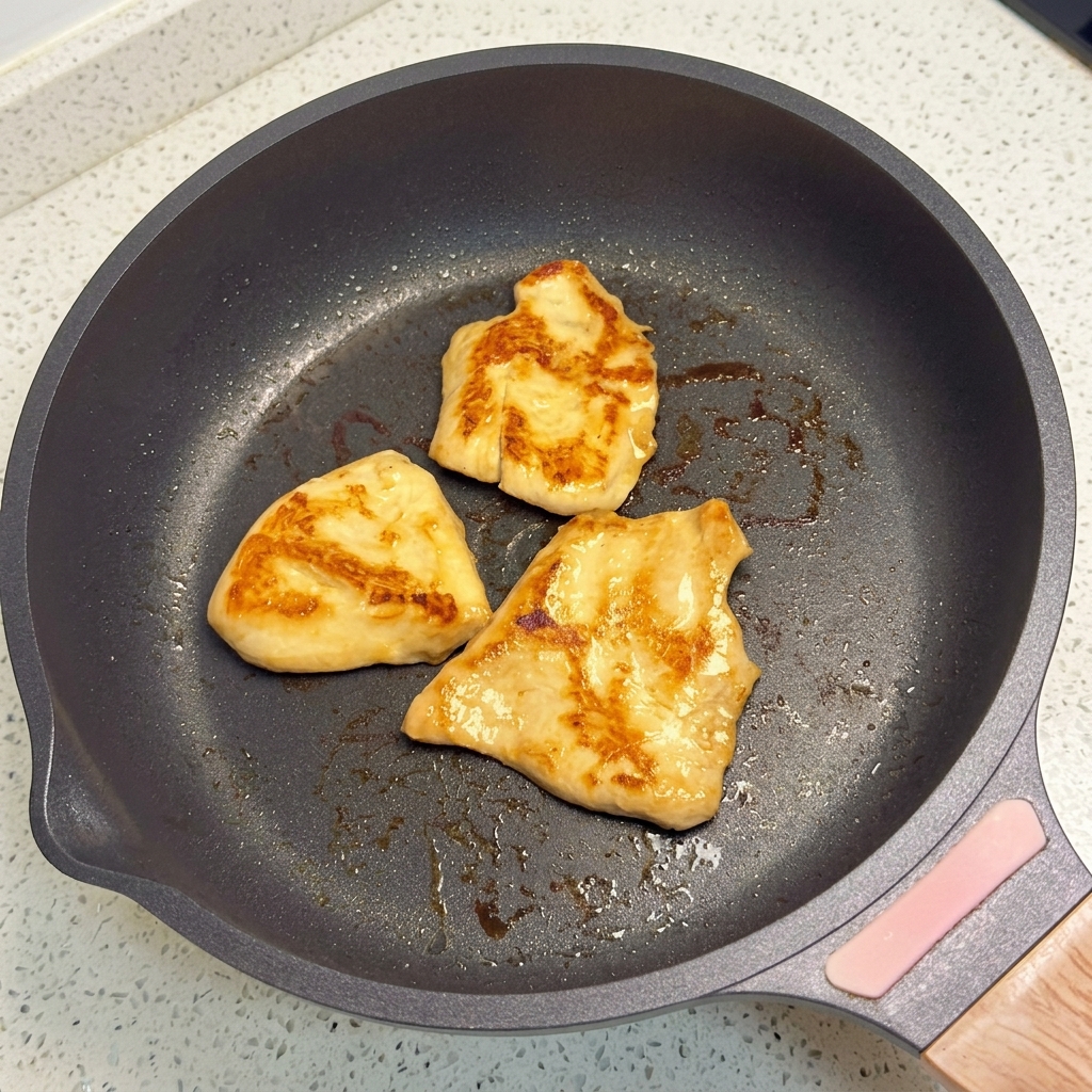 Morceaux de poulet en train de frire dans une poêle à fond plat jusquà lobtention dune couleur dorée.