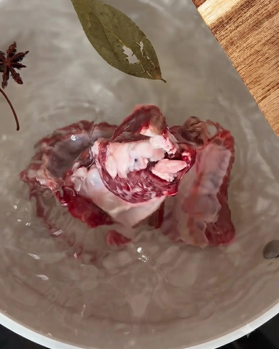 Côtes de porc mijotant dans une casserole deau avec de lanis étoilé et une feuille de laurier flottant à la surface.
