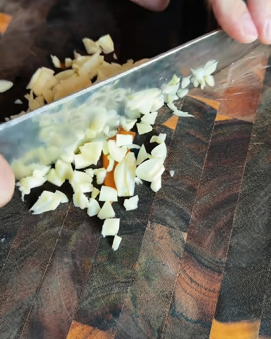 Morceaux dail fraîchement émincés éparpillés sur une planche à découper en bois foncé.
