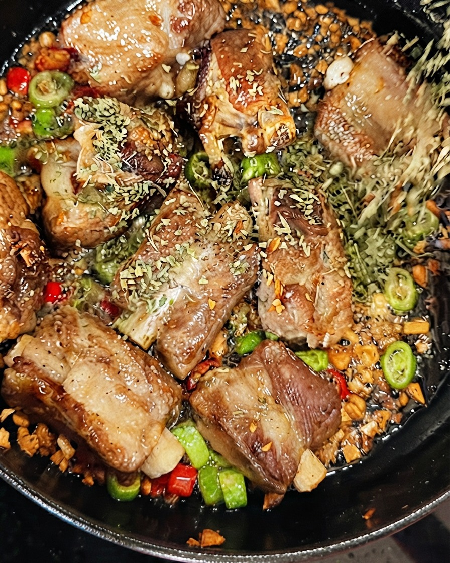 Persil séché saupoudré sur les côtes de porc tandis que du vin blanc sec est versé dans la poêle grésillante.