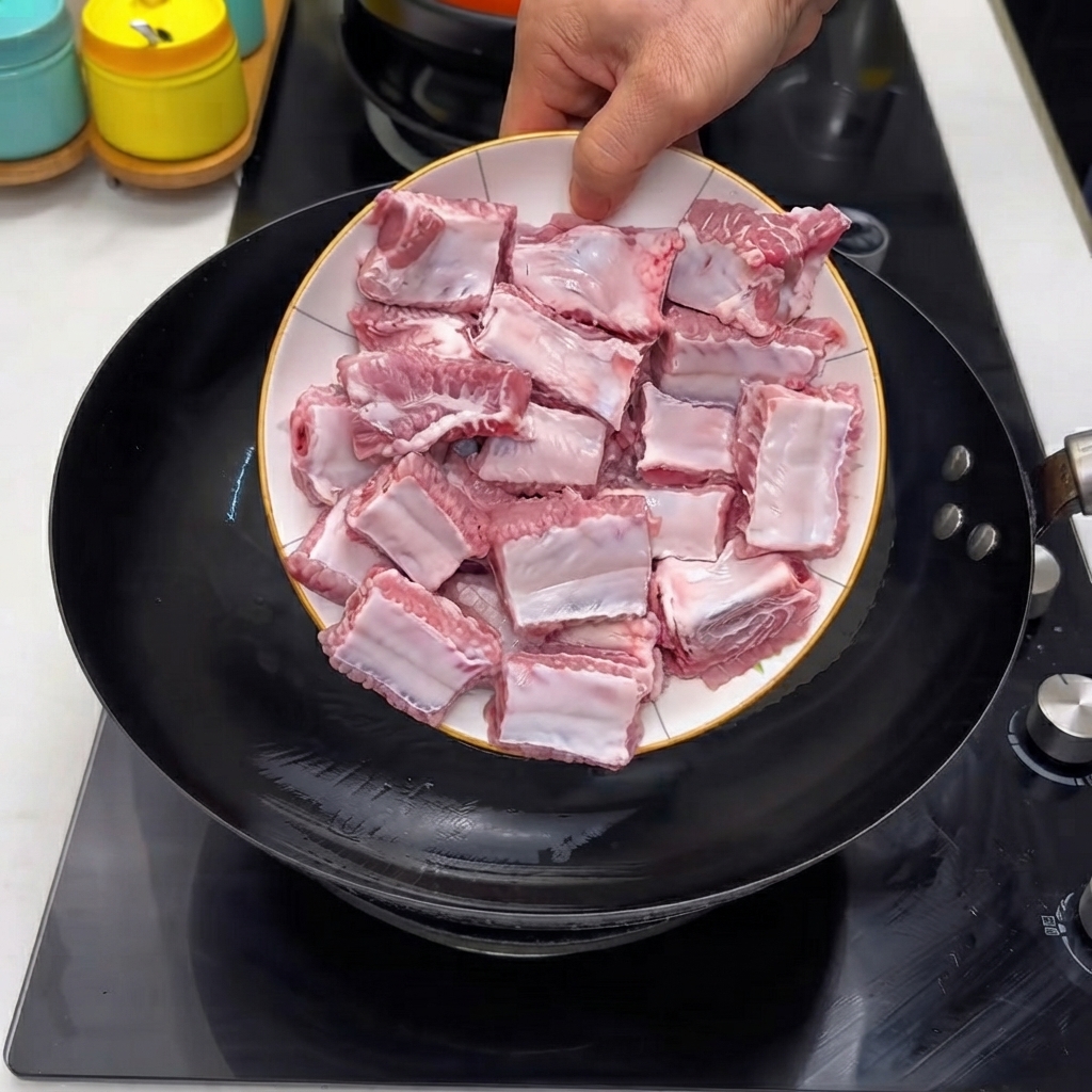 Des côtes de porc crues versées dune assiette blanche dans un wok noir chaud.