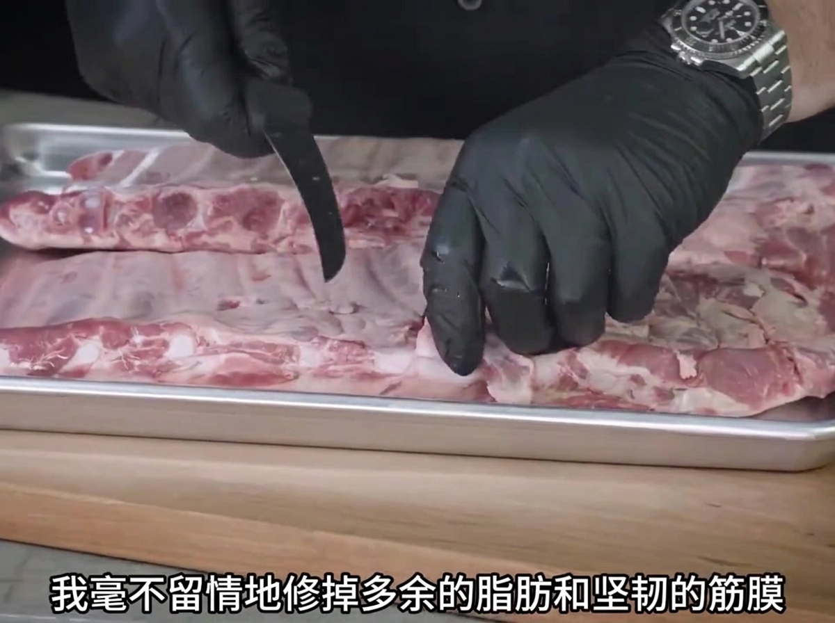 Une paire de mains gantées utilisant un couteau pour parer lexcès de gras sur des travers de porc crus posés sur un plateau en métal.