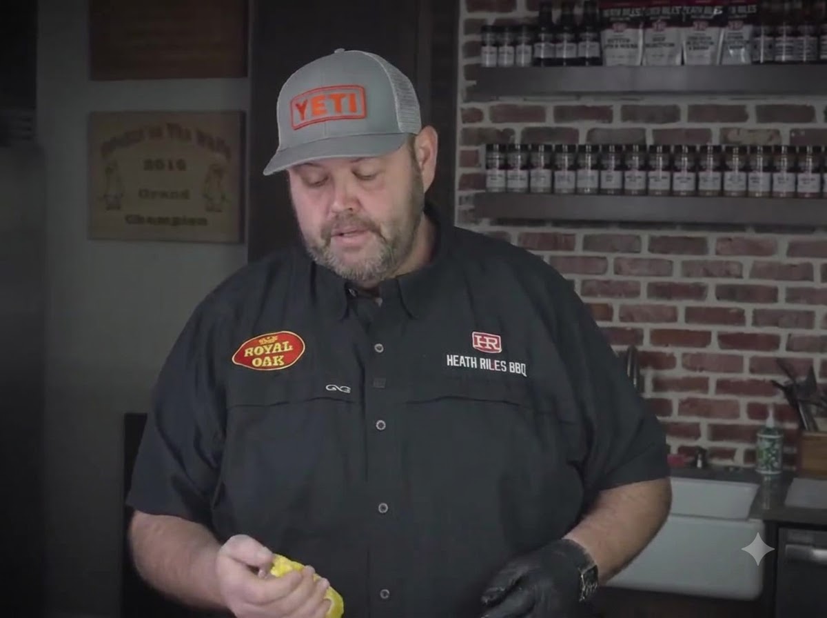 Un chef tenant une bouteille de moutarde jaune tout en préparant des ribs dans une cuisine.
