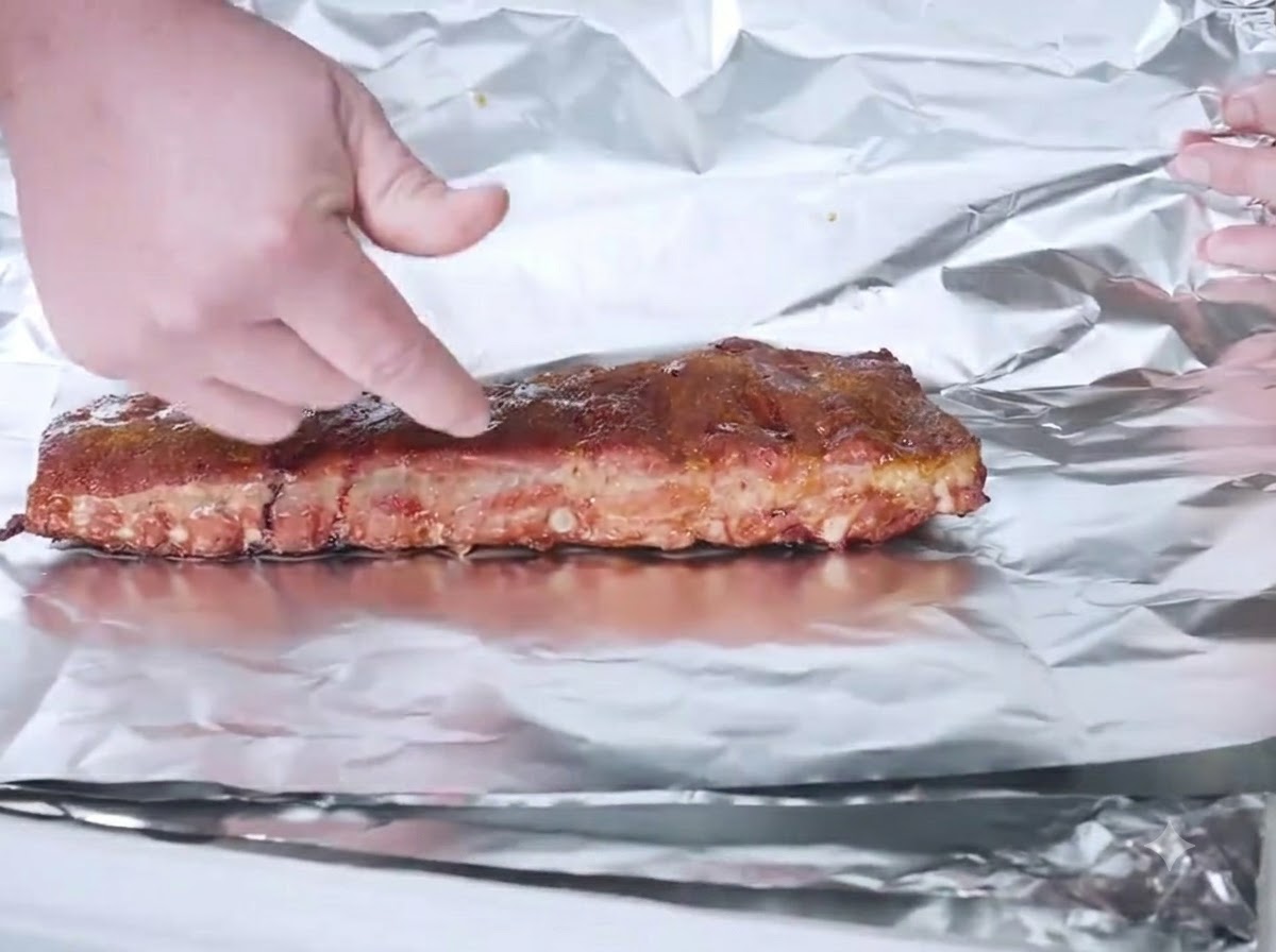 Des ribs fumés posés sur une feuille daluminium prêts à être emballés.