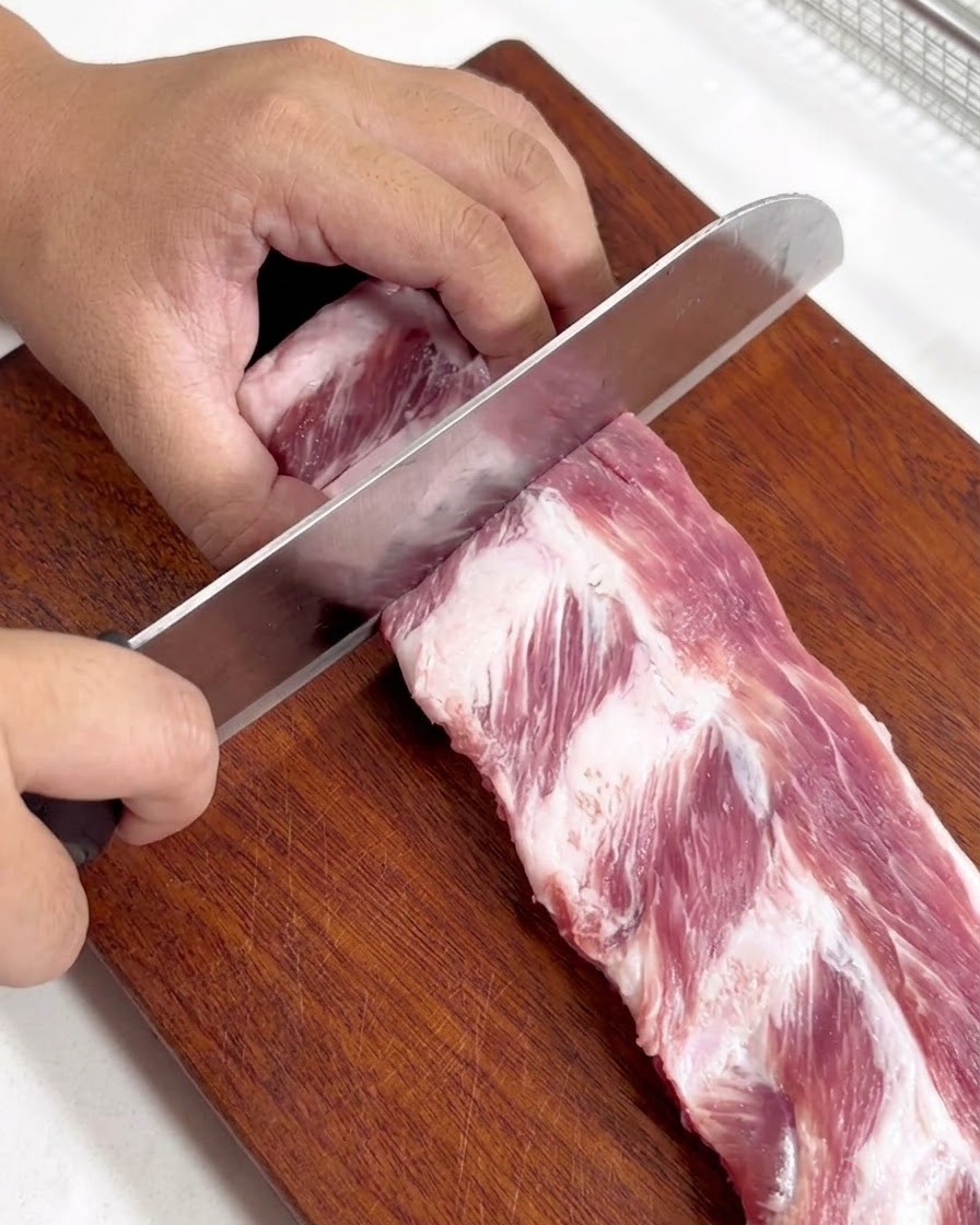 Un rack de travers de porc crus découpés en morceaux individuels sur une planche à découper en bois.
