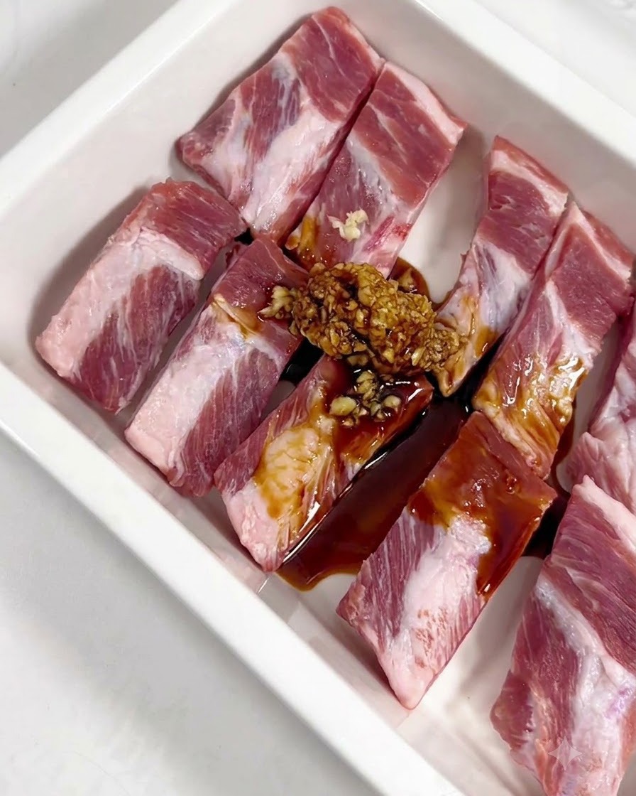 De lail émincé, de la sauce soja, de la sauce huître, du miel et des condiments en poudre versés sur des travers de porc crus dans un plateau blanc.