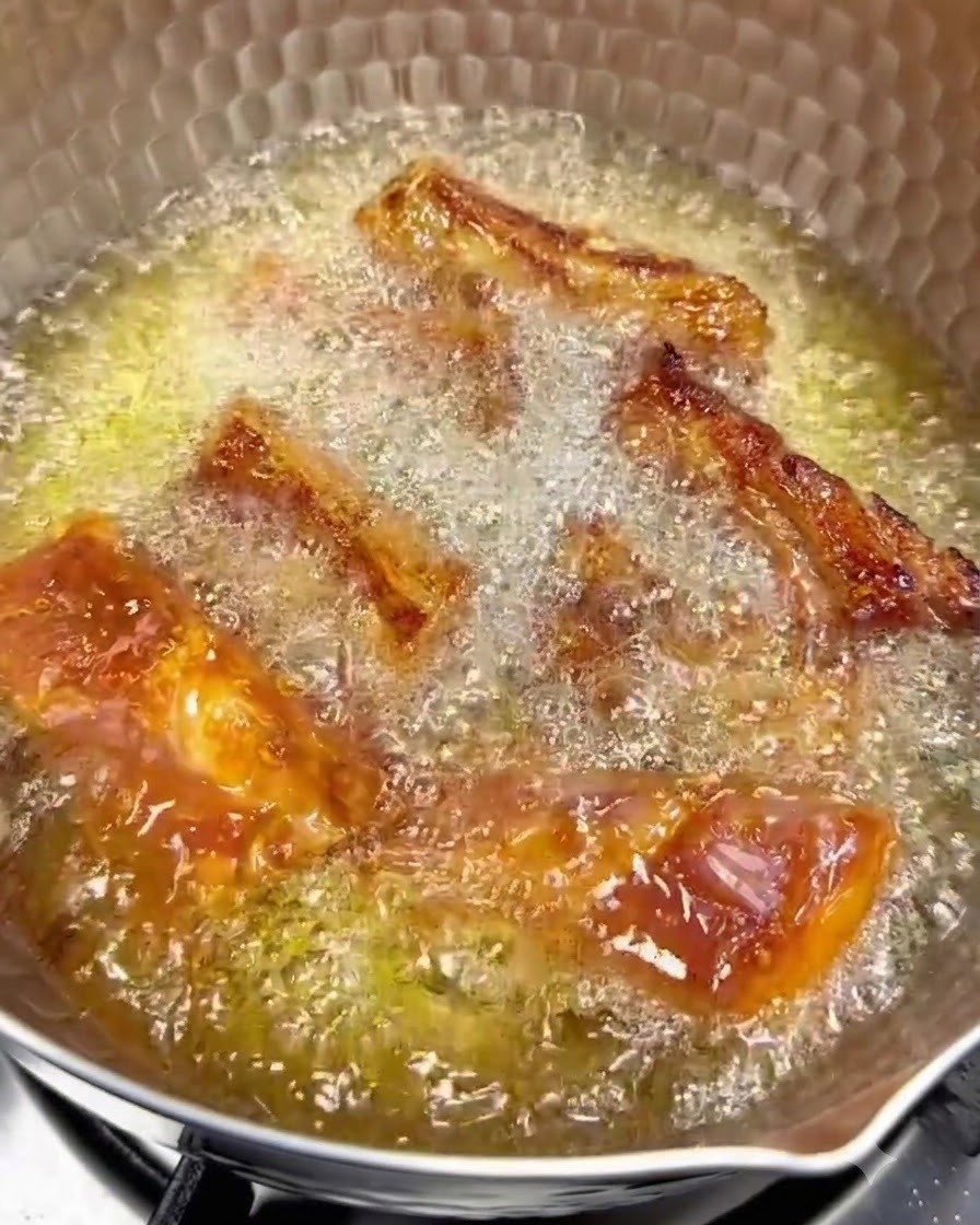 Des travers de porc en train de frire dans lhuile chaude à feu doux avec des surfaces dorées visibles.