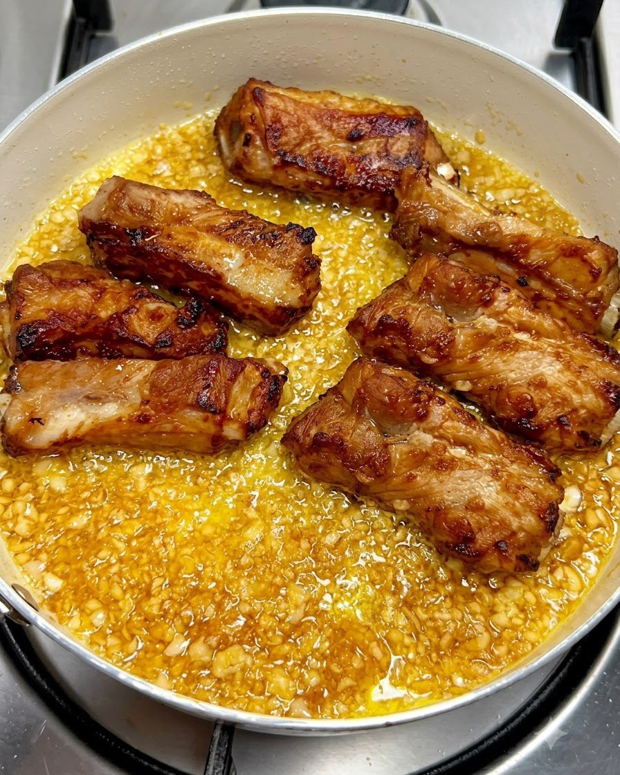 Des travers de porc frits dorés disposés soigneusement à lintérieur dune poêle remplie dune sauce bouillonnante au beurre à lail.