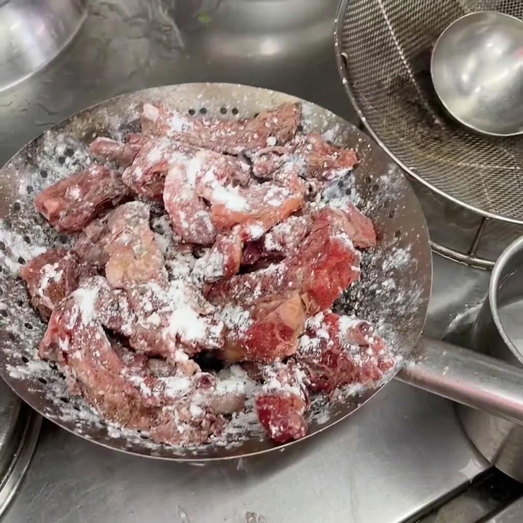 Côtes de porc marinées reposant dans une passoire en métal avec un enrobage blanc visible de fécule.