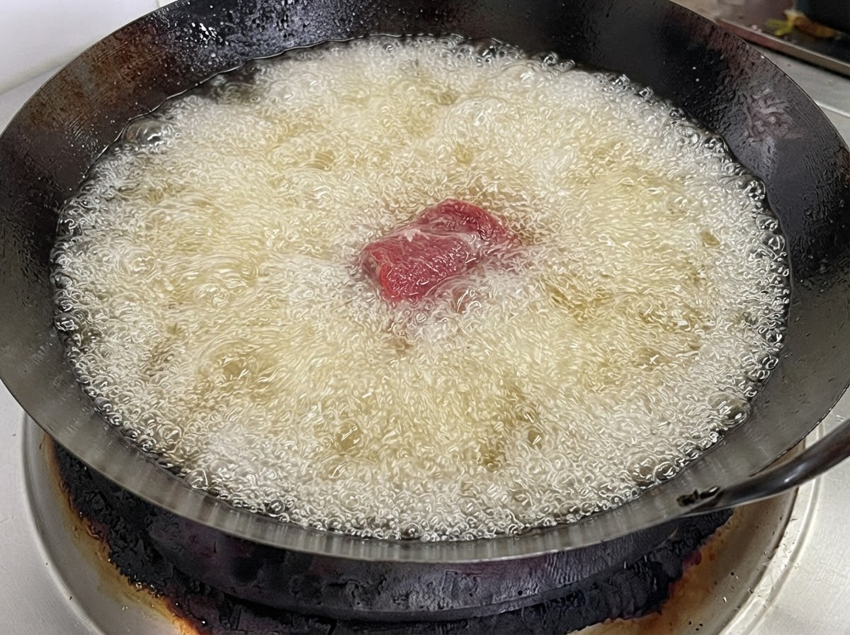 Un seul morceau de côte de porc jeté dans un wok rempli dhuile de friture chaude et bouillante.