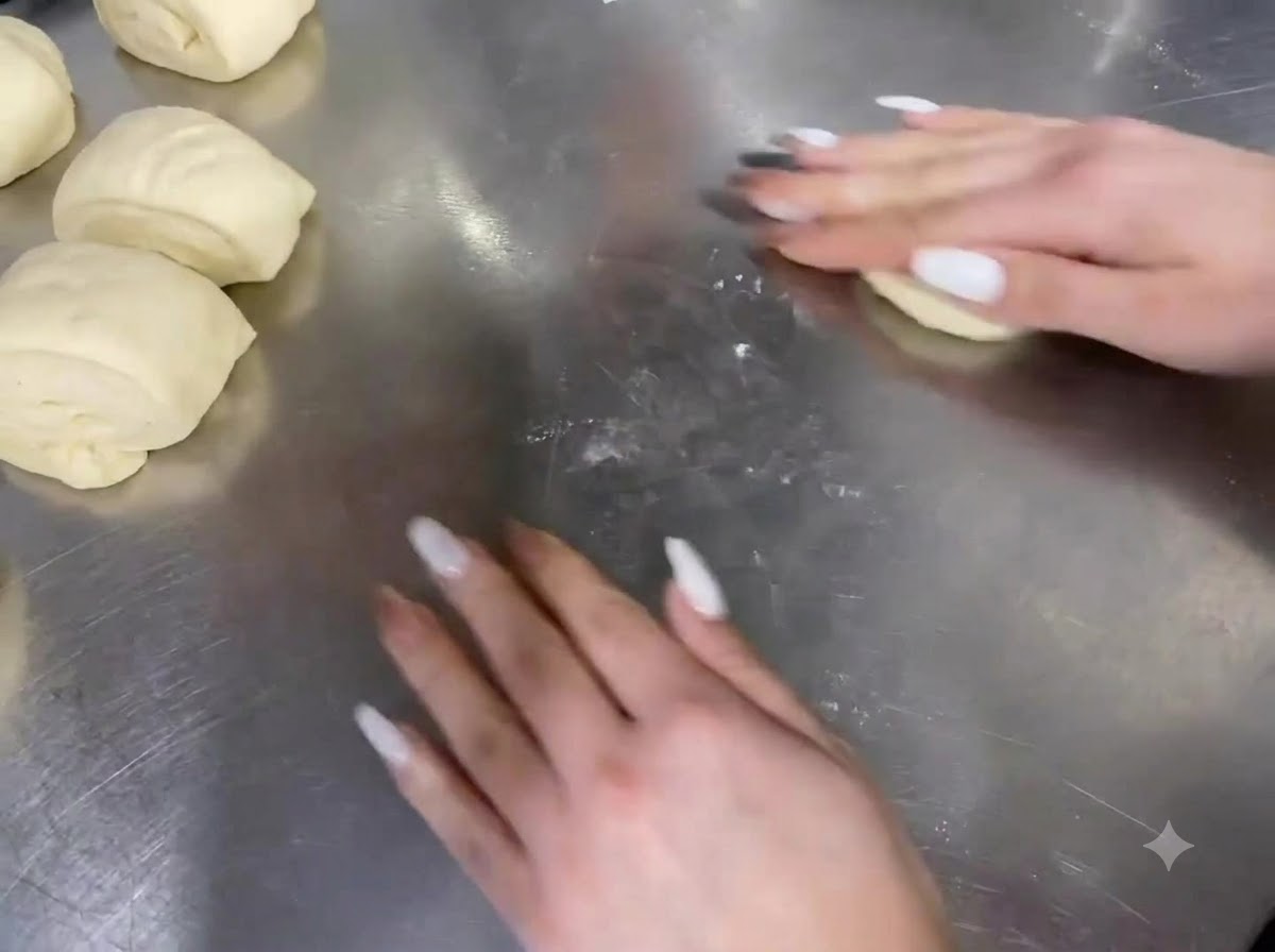 Mains roulant des portions de pâte sur un plan de travail en acier inoxydable.
