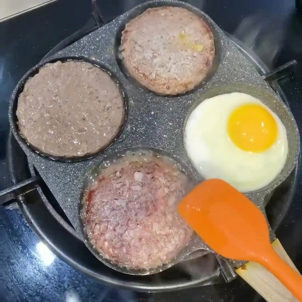 Steaks de burger retournés avec une spatule orange à côté dun œuf en train de frire dans une section de la poêle.