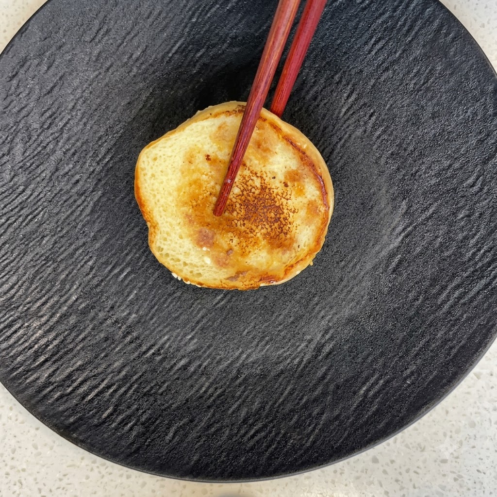 Une moitié de pain à burger toasté reposant sur une assiette noire texturée avec des baguettes.
