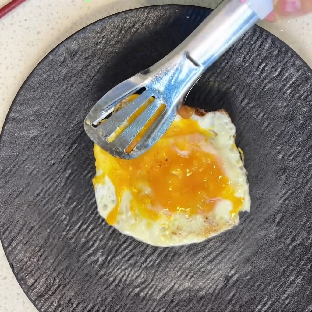 Un œuf fraîchement frit positionné avec précaution sur les tomates tranchées à laide de pinces en métal.