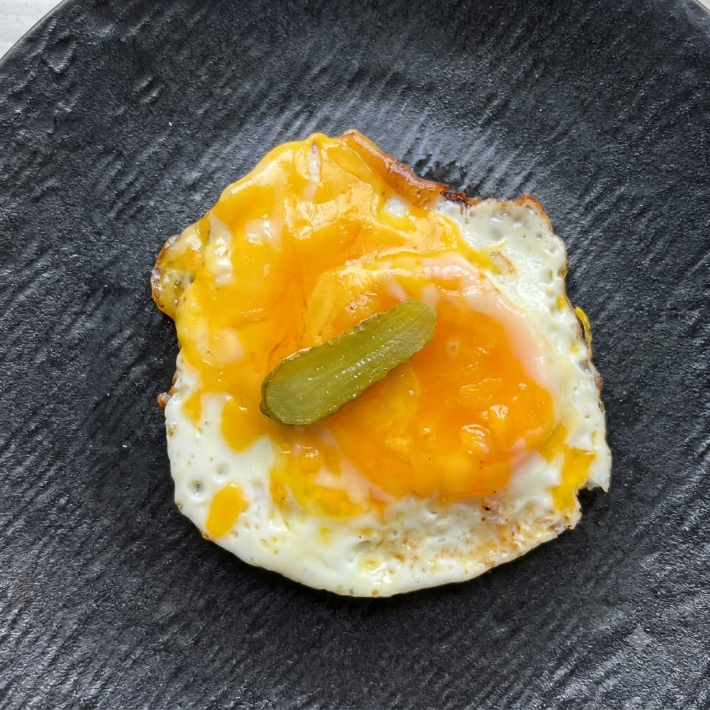 Une seule petite tranche de cornichon placée au centre sur lœuf au plat et le fromage.