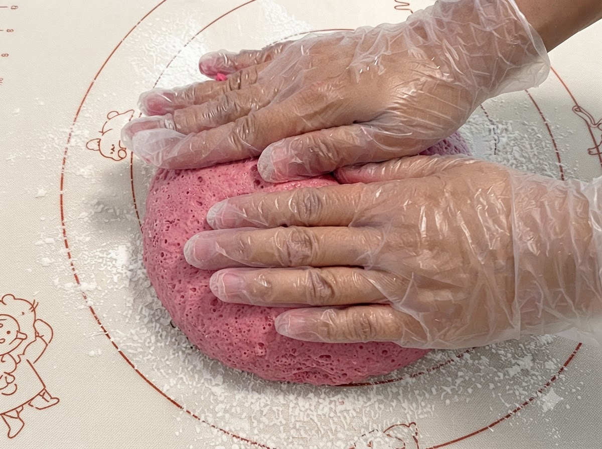 Pâte rose fermentée pressée et pétrie sur un tapis en silicone.