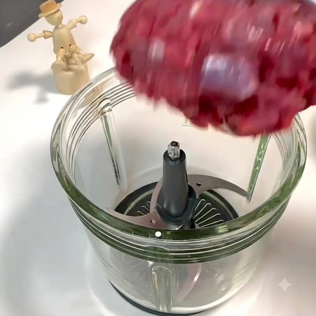Morceaux de filet de bœuf et de poitrine de porc tombant dans le récipient en verre ouvert dun robot culinaire au-dessus des lames en métal.