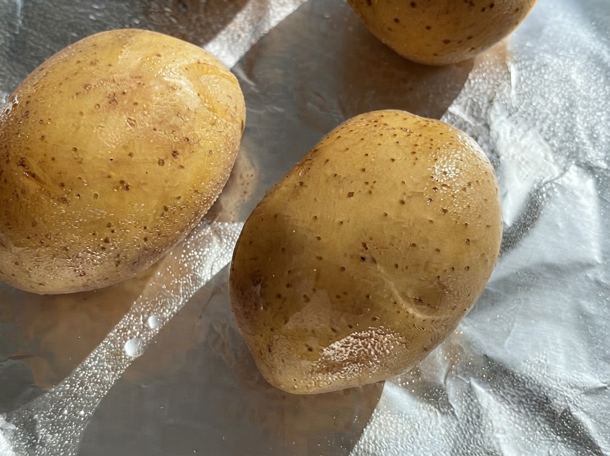 Pommes de terre entières crues badigeonnées dhuile sur une feuille de papier aluminium.