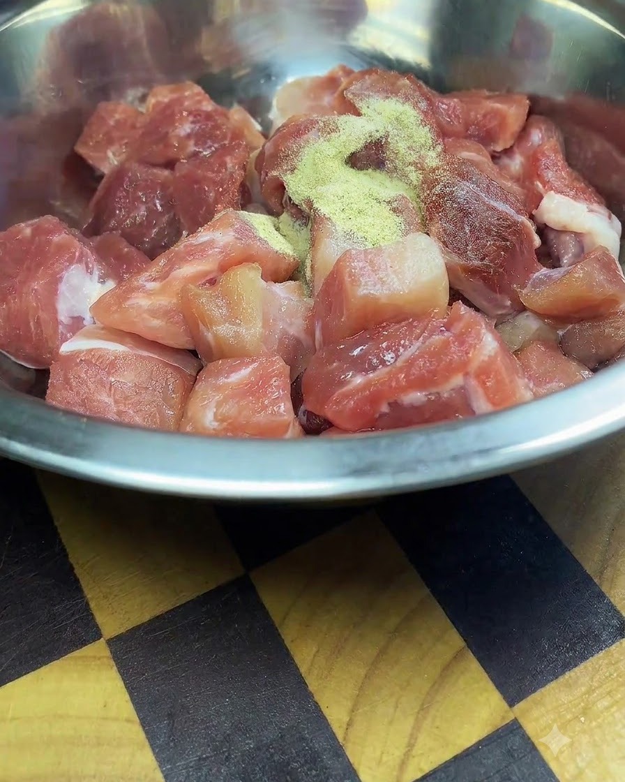 Morceaux de porc frais coupés dans un bol en acier inoxydable saupoudrés dassaisonnements et de fécule de maïs.