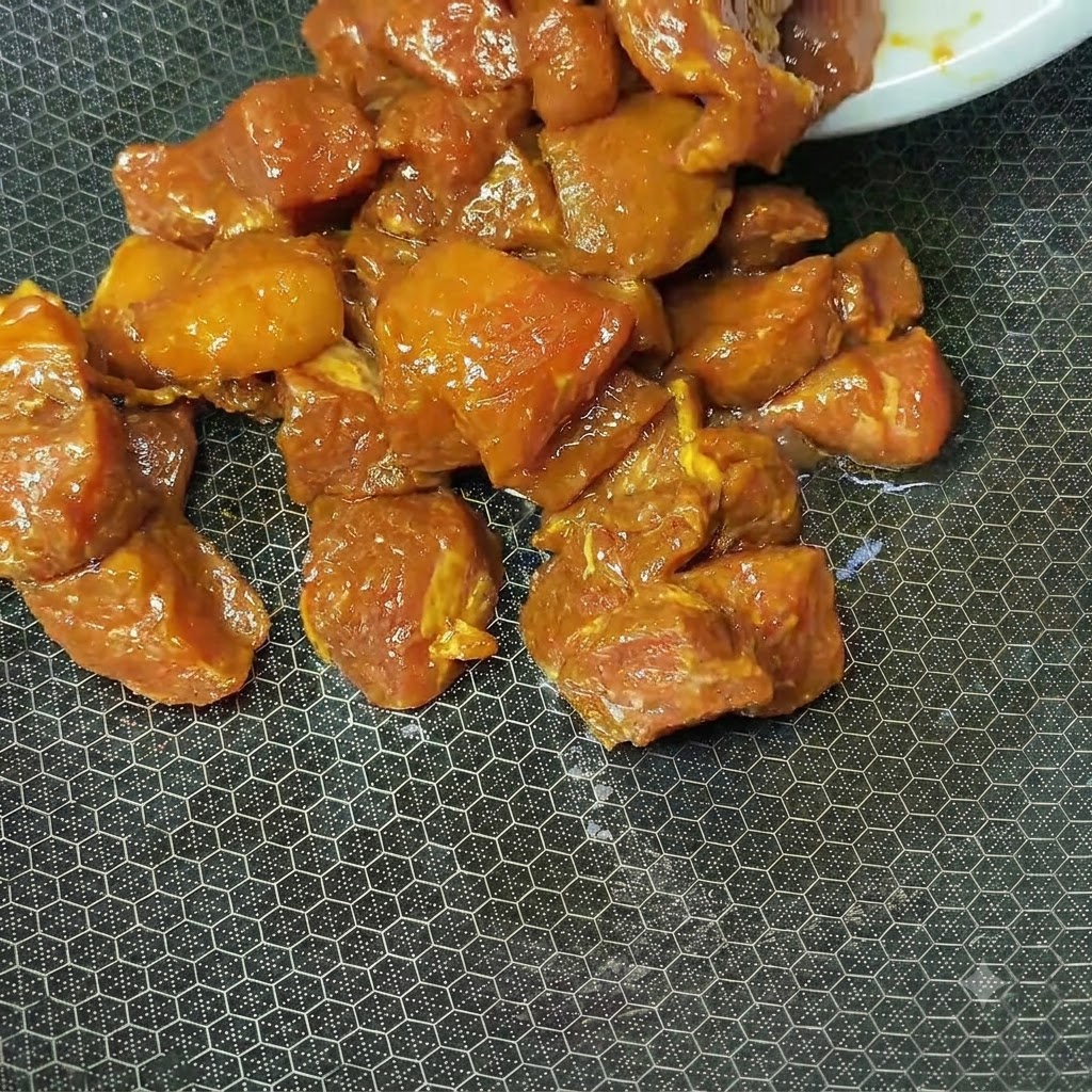 Cubes de porc marinés brun rougeâtre cuisant dans un wok chaud texturé.