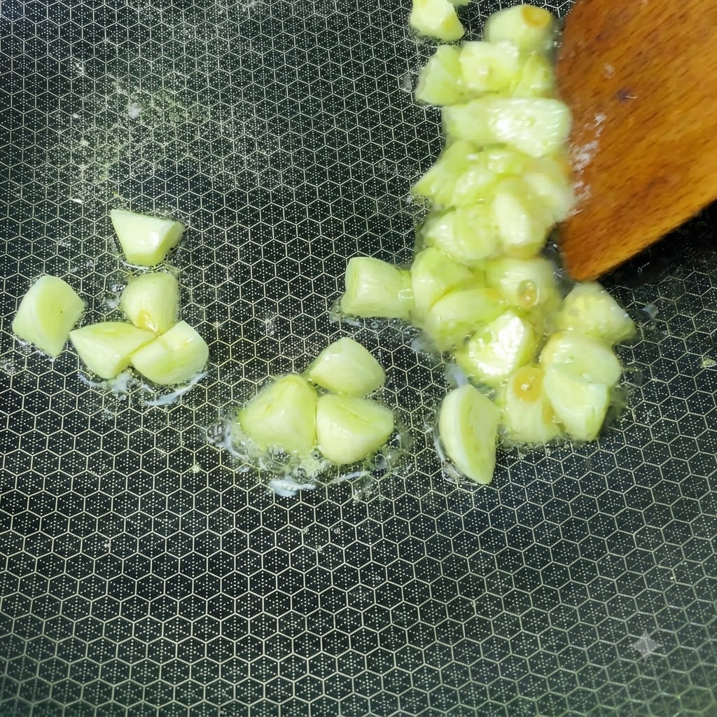 Gousses dail fraîchement hachées grésillant dans de lhuile chaude à lintérieur dun wok remué avec une spatule en bois.