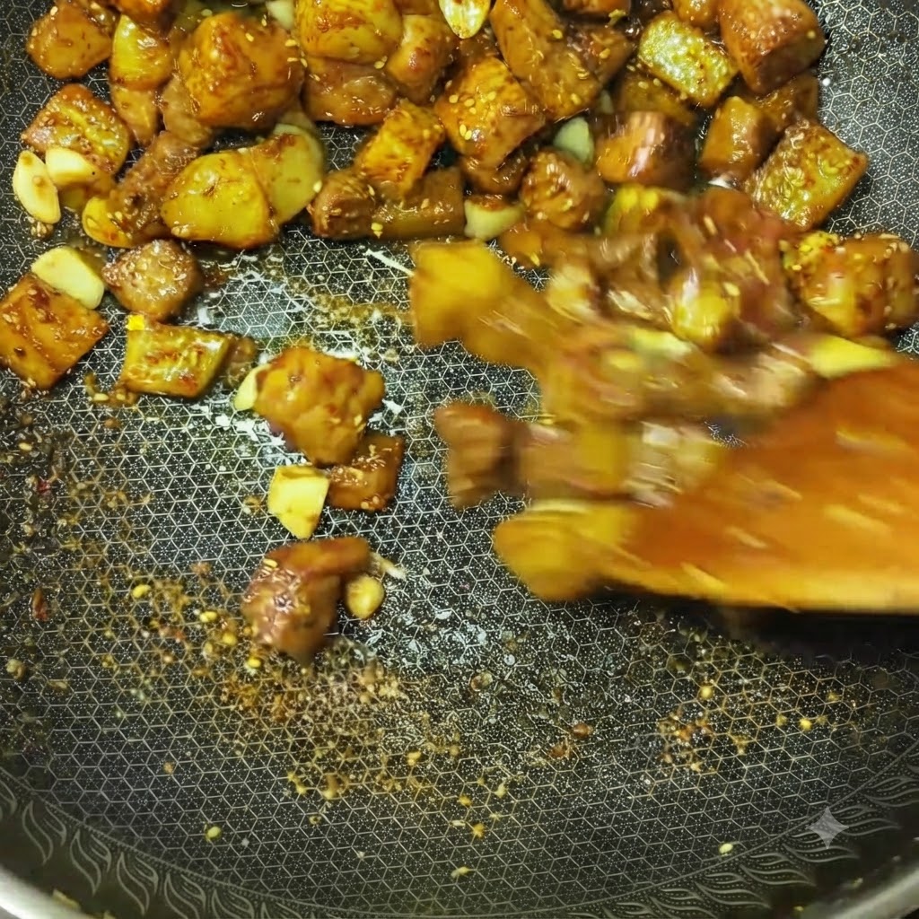 Cubes de viande et morceaux de pommes de terre sautés rapidement dans un wok avec des épices et des assaisonnements visibles.