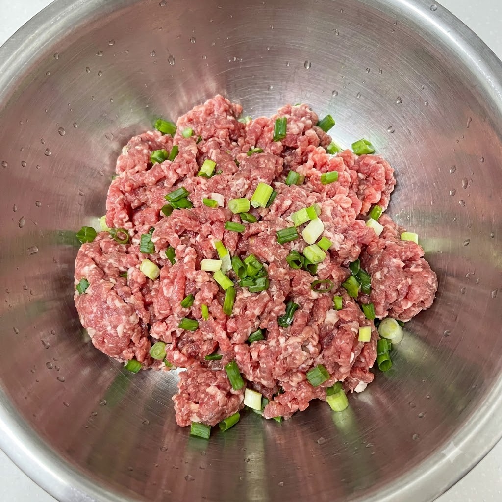 Des oignons verts hachés fraîchement déposés sur de la viande hachée dans un bol en inox.