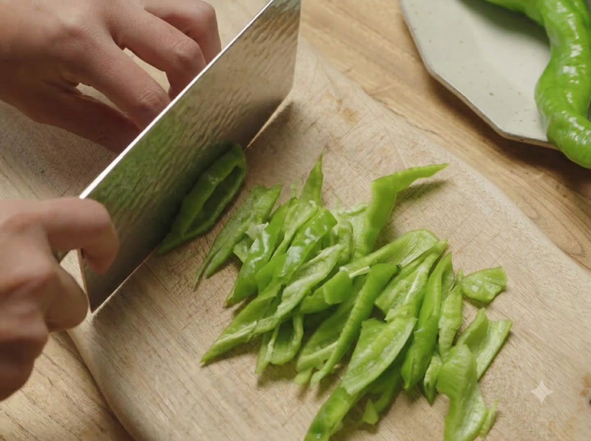 Des poivrons verts spiralés coupés en morceaux biseautés sur une planche en bois à laide dun couperet.