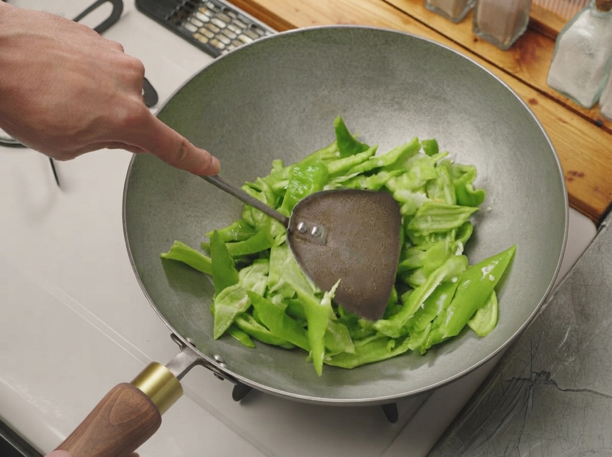 Des poivrons verts coupés mélangés avec une spatule en métal dans un wok chaud et sec.