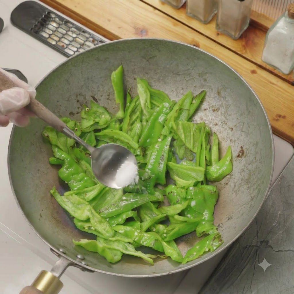 Une pincée de sel ajoutée aux poivrons verts tranchés en train de sauter à sec dans un wok.