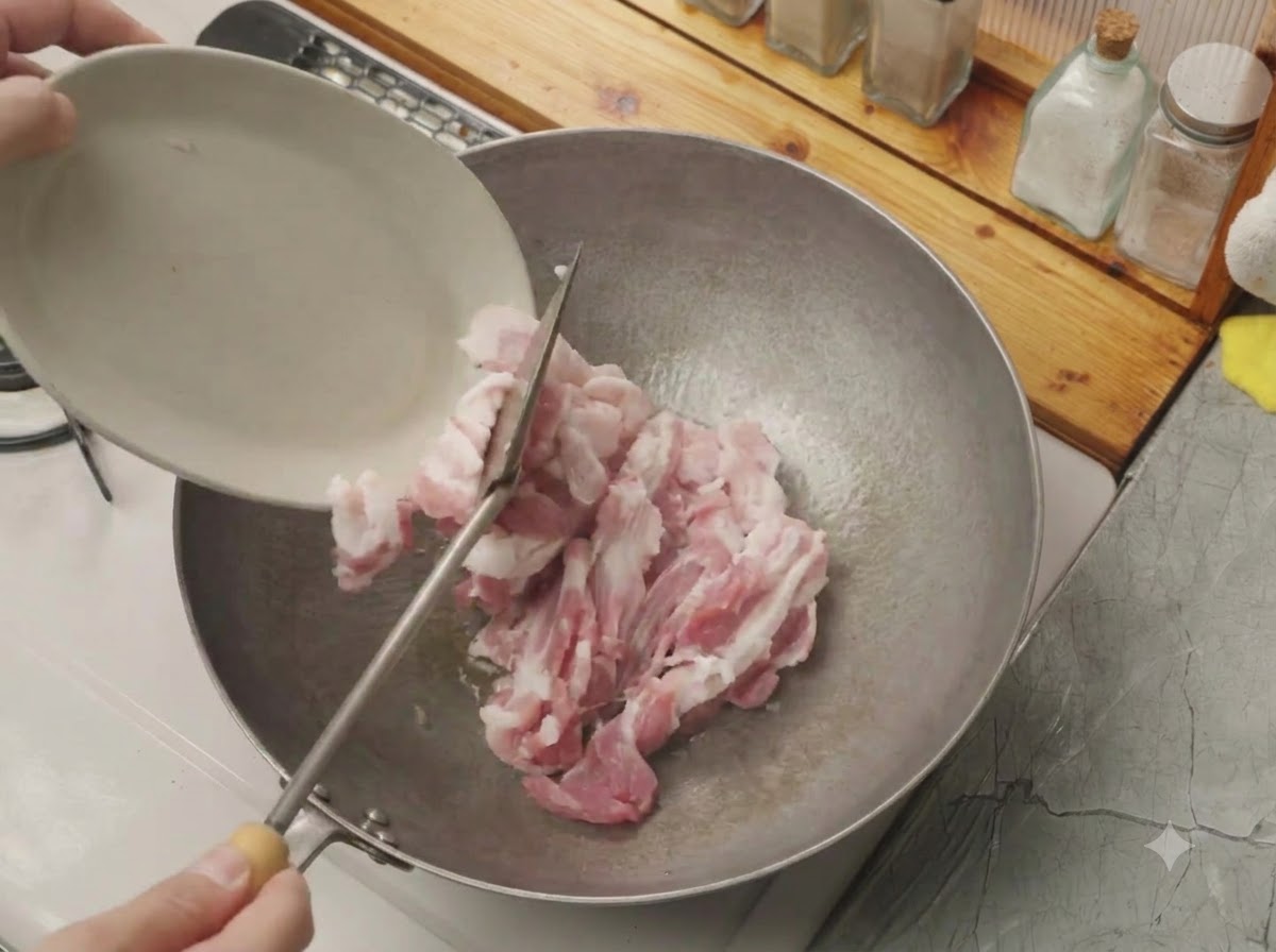 Des lanières de poitrine de porc crue glissées dune petite assiette blanche vers un wok chaud.