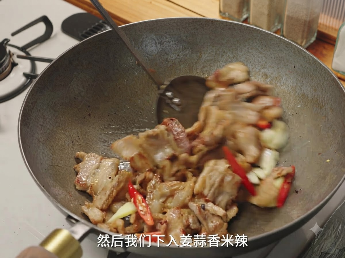 Du gingembre, de lail et des piments rouges mélangés avec des morceaux de porc dorés dans un wok.