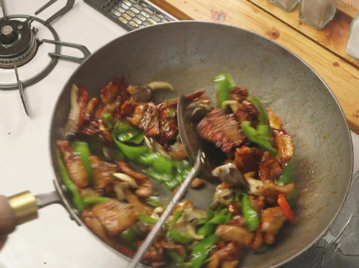 Une spatule mélangeant des poivrons verts, des champignons et de la poitrine de porc ensemble dans un wok chaud.