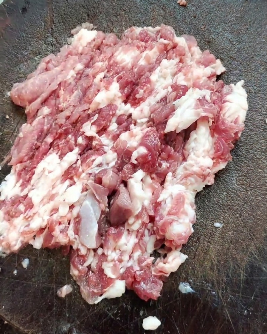 Un couteau de boucher posé sur un tas de viande dépaule de porc fraîchement hachée sur une planche en bois texturée.