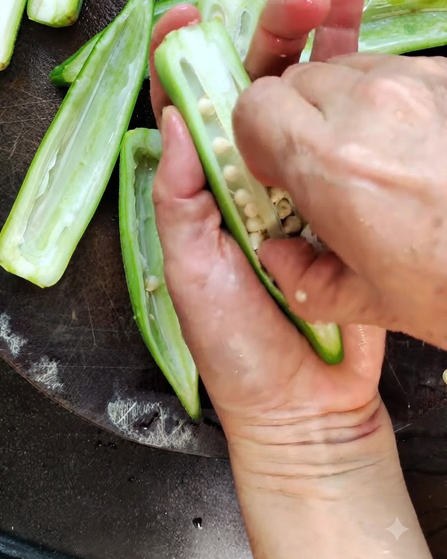 Un couteau de cuisine tranchant au milieu une gousse de gombo vert frais sur une planche en bois.