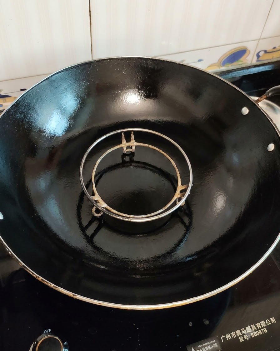 Un panier vapeur vide placé à lintérieur dun grand wok noir prêt pour la cuisson.