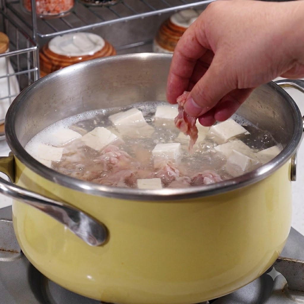 Une main plaçant des tranches de porc marinées dans une casserole contenant du bouillon bouillant, du tofu et des fruits de mer.