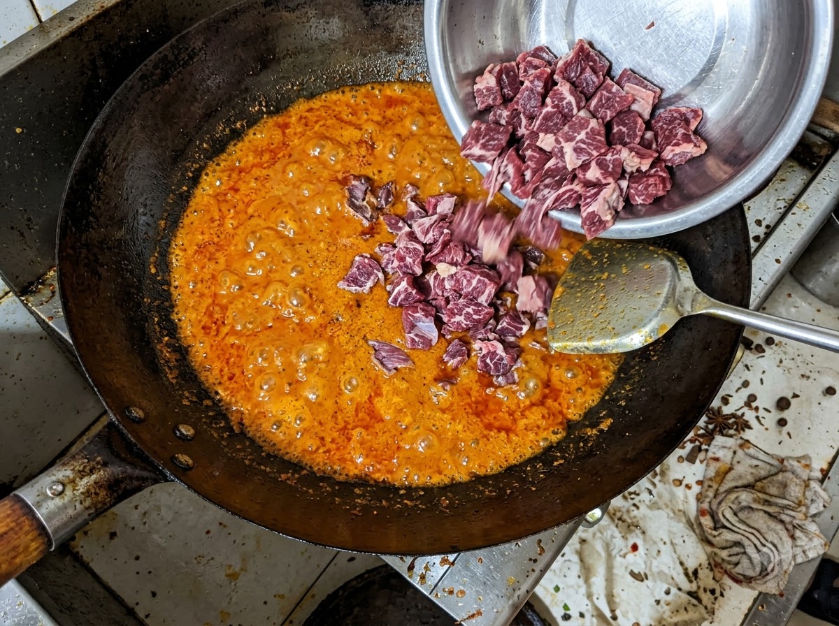 Morceaux de bavette de bœuf versés dun bol en métal dans un mélange dhuile de piment rouge frémissante dans un wok.