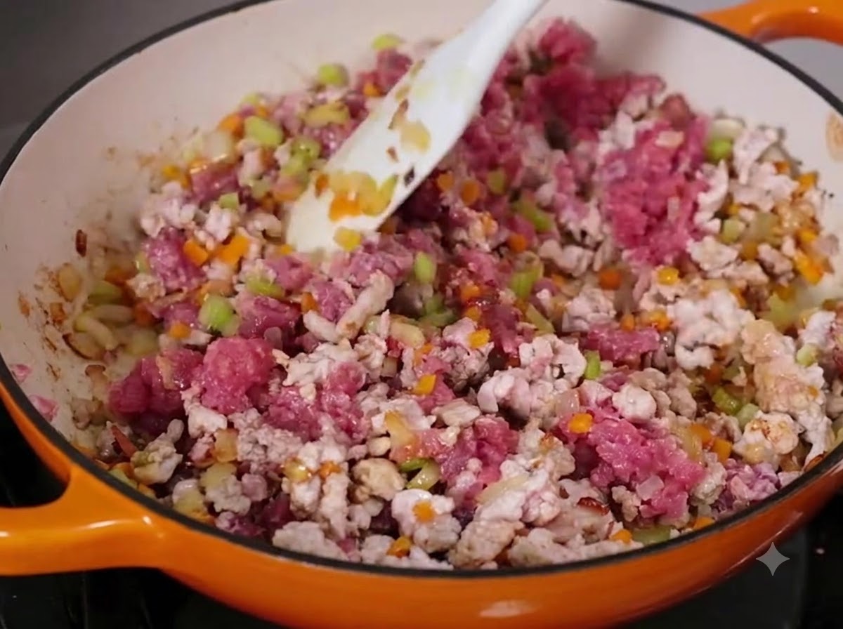 Du bœuf et du porc hachés mélangés avec des légumes en dés dans une grande poêle à laide dune spatule blanche.