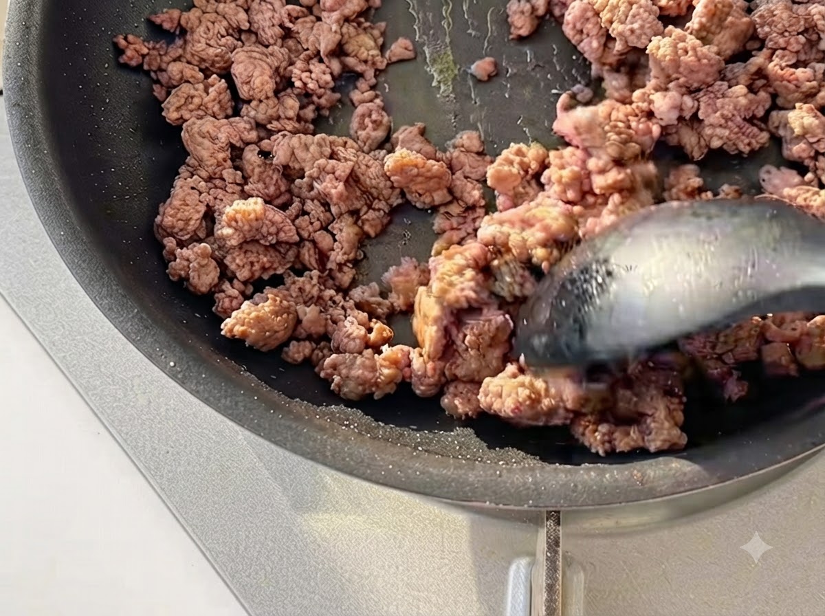 Du bœuf haché sauté à la spatule dans une poêle noire jusquà ce quil soit légèrement dorés.
