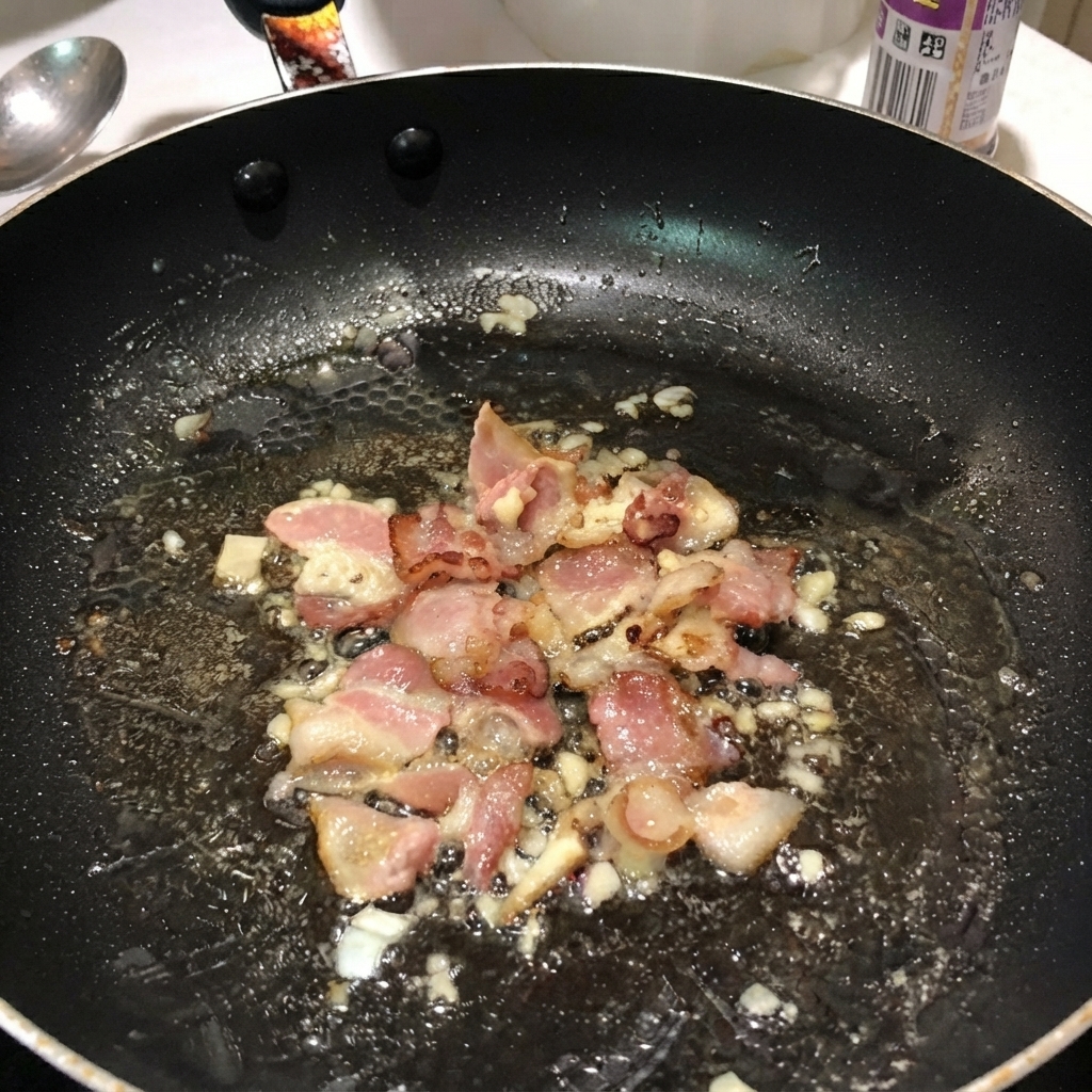 Des penne bouillies mélangées avec du bacon et des oignons à lintérieur dune poêle noire.
