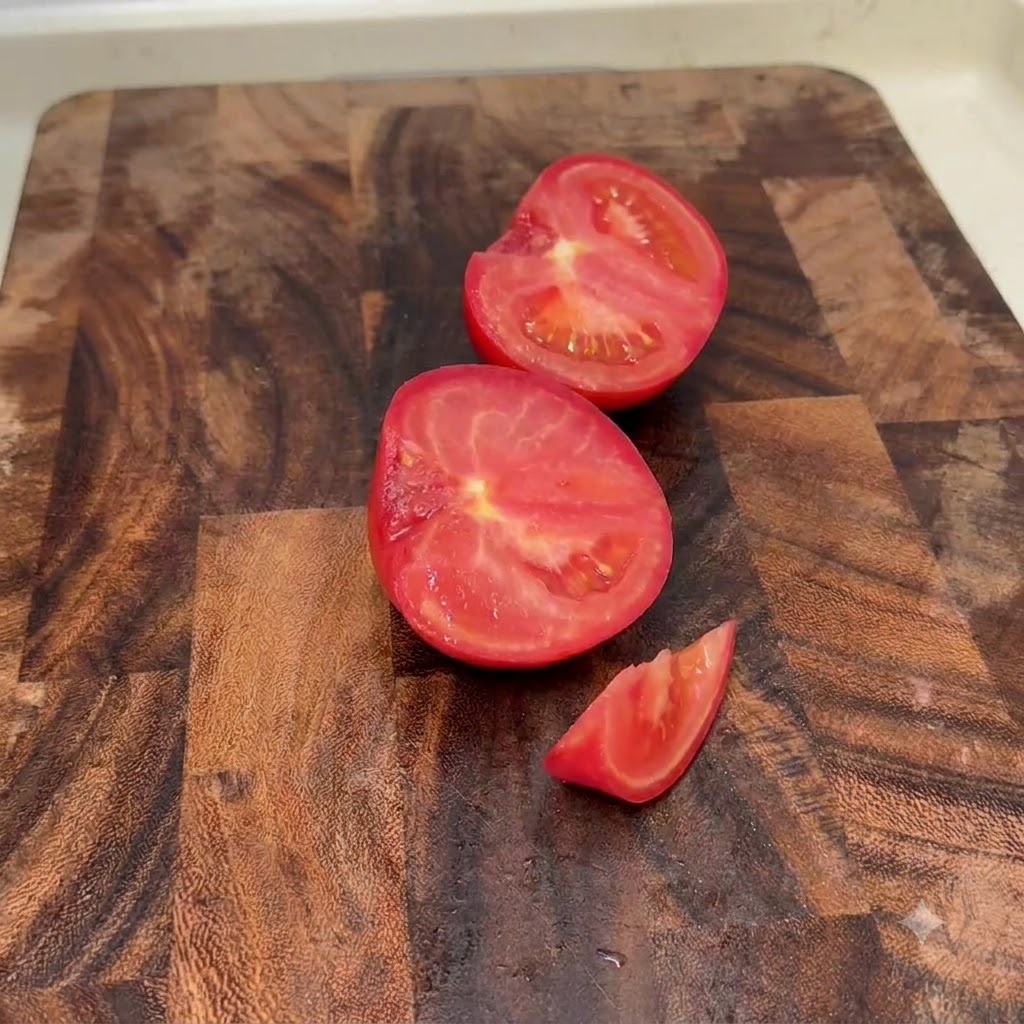 Fraîches tomates coupées en deux et en petits morceaux sur une planche à découper en bois.