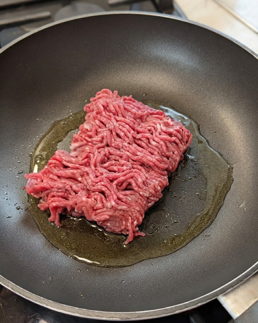 Du bœuf haché cru dans une poêle avec de lhuile, des oignons et de lail.
